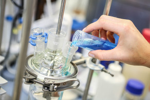 A hand fills a turquoise blue liquid into another glass vessel in the laboratory.